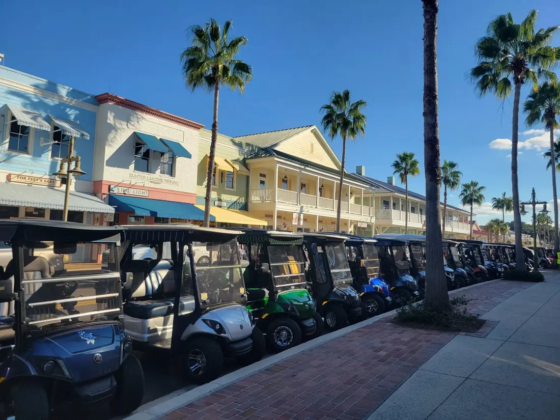 Two-story shops and restaurants along a palm-lined town square street lined with golf carts in Sumter County